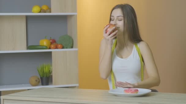 Chica en la mesa felizmente comer una manzana y deslizar su pan de jengibre — Vídeo de stock