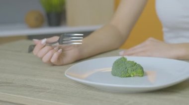 Kız bir masaya oturur ve diyete yapışmış brokoli yer.