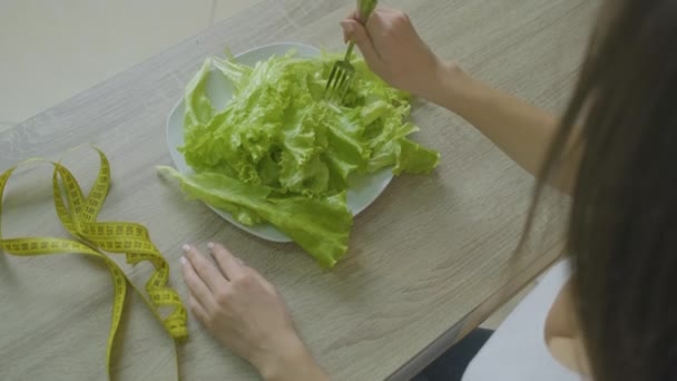 Žena sedí u stolu a jí zelí listy lpí na dietě