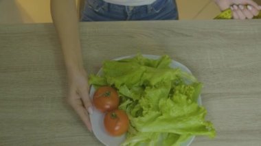 Kadın masaya oturur ve sebzelerini toplar.