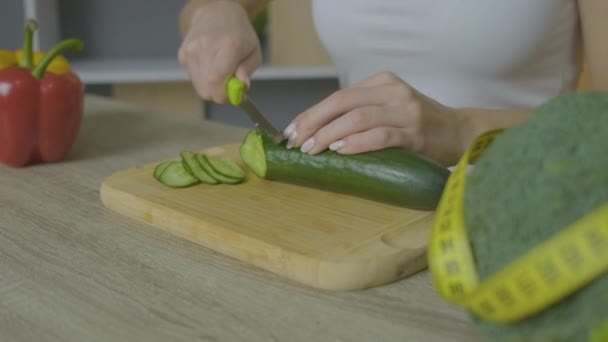 En vit kvinna sitter vid ett bord och skär en gurka. Stäng ram — Stockvideo