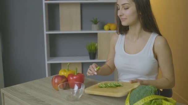 Lány ül az asztalnál mozog szeletelt uborka egy tányérba — Stock videók