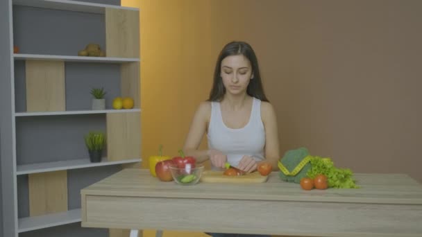 Blank meisje kijkt naar tafel en snijdt tomaat — Stockvideo