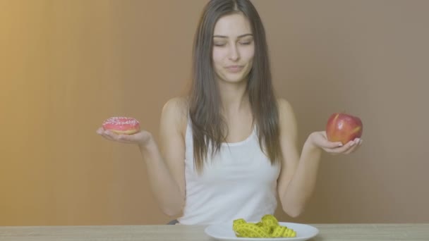 Κορίτσι με λεπτή φιγούρα που κρατάει ένα ντόνατ και ένα μήλο — Αρχείο Βίντεο