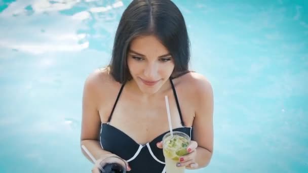 Женщина в шляпе расслабляется в бассейне с космополитическим коктейлем — стоковое видео