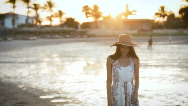 Menina ao pôr do sol usa um chapéu e olha para o mar — Vídeo de Stock