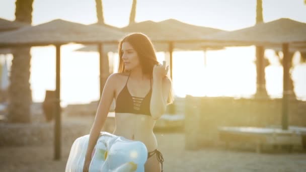 Menina com um colchão caminha na praia perto de palmeiras — Vídeo de Stock