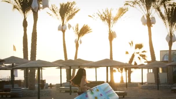 Ragazza con materasso che corre sulla spiaggia sullo sfondo di palme — Video Stock