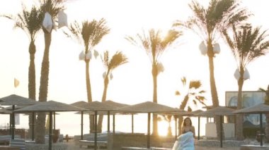 Plajda palmiye ağaçlarının arkasında koşan şilteli bir kız.