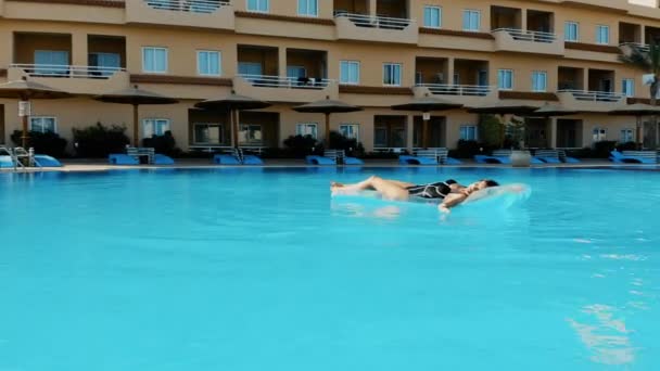 Um drone voando sobre uma piscina no Egito, onde uma menina está deitada em um colchão — Vídeo de Stock