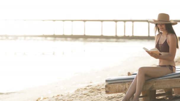 Das Mädchen sitzt auf einem Liegestuhl am Meer und liest ein Buch — Stockvideo