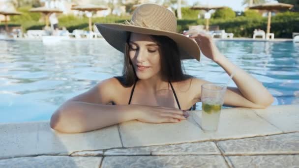 Woman in hat relaxing at pool with cosmopolitan cocktail — Stock Video