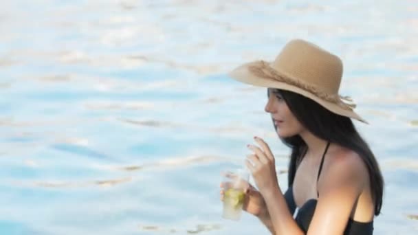 Vrouw met hoed ontspannen aan het zwembad met kosmopolitische cocktail — Stockvideo