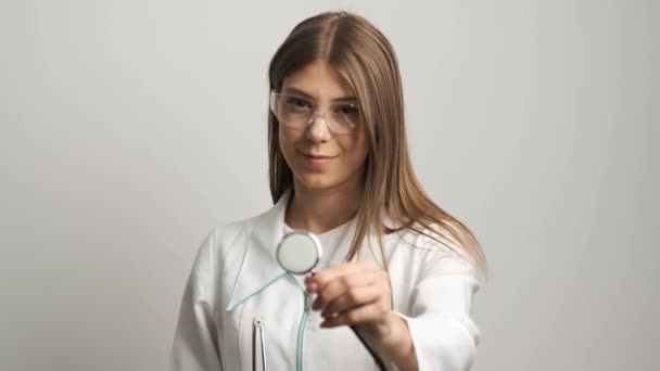 Hermosas mujeres médico de apariencia caucásica sonríe a la cámara y sostiene un estetoscopio. Sanidad — Vídeos de Stock