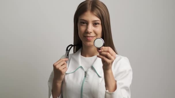 Kafkas görünümlü güzel kadın doktor kameraya gülümser ve bir stetoskopi tutar. İlaç. Sağlık — Stok video