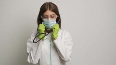 Eldivenli beyaz kadın doktor steteskop takıyor ve kameraya yaklaşıyor. Sağlık
