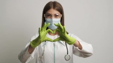 Eldivenli ve steteskoplu harika doktor kameraya bakarak kalp şeklini gösteriyor.