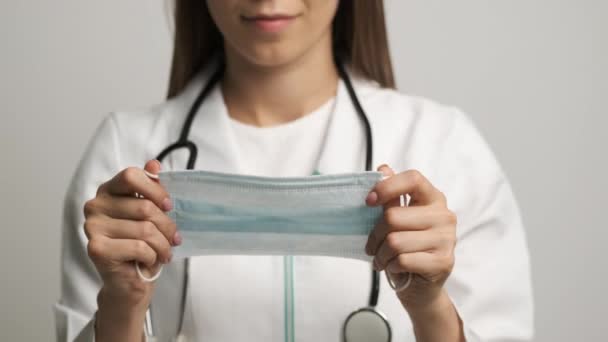 Mulheres médico em um casaco branco segurando uma máscara sorrindo para a câmera — Vídeo de Stock