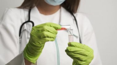 Maskeli ve eldivenli kız doktor test tüpleri tutuyor ve bir test tüpünden diğerine sıvı döküyor. Sağlığa. İlaç.