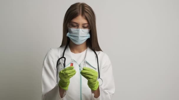マスクと手袋の少女医師は、試験管を保持し、ある試験管から別の試験管に液体を注ぎます。健康。医学 — ストック動画