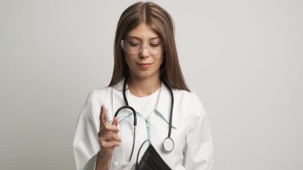 Девушка-врач кавказской внешности держит маску и антисептик придерживается гигиены — стоковое видео