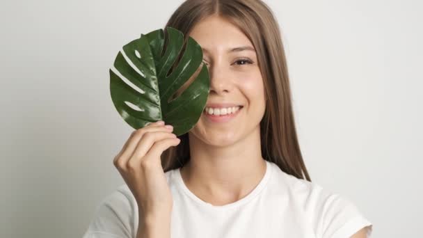 Hermosa chica de aspecto caucásico con hojas verdes posando delante de la cámara — Vídeo de stock