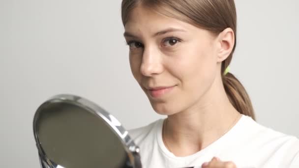 Девушка смотрит в зеркало на фоне зеленого цветочного горшка — стоковое видео