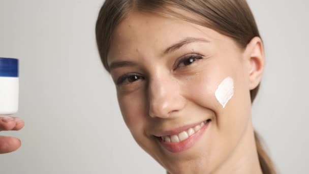 Девушка с белой внешностью наносит крем на лицо — стоковое видео