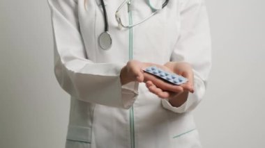 Kadın doktor kameranın önünde tedavi haplarını tutuyor.