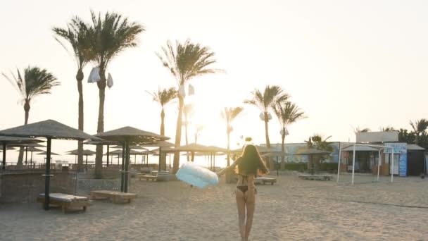 Dziewczyna z materacem biegająca po plaży na tle palm — Wideo stockowe