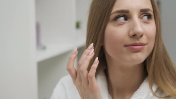 Meisje brengt crème op gezicht in lichte kamer — Stockvideo
