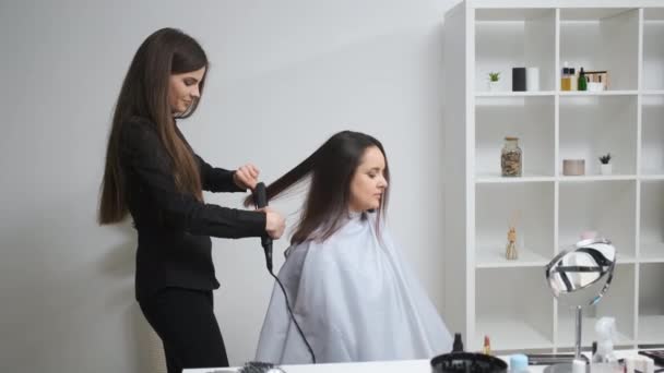 Chica alisando su cabello con rizador en un salón de belleza — Vídeos de Stock