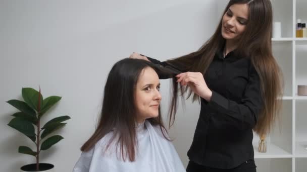 Κορίτσι ισιώνει τα μαλλιά της με σίδερο για μπούκλες σε ένα σαλόνι ομορφιάς — Αρχείο Βίντεο