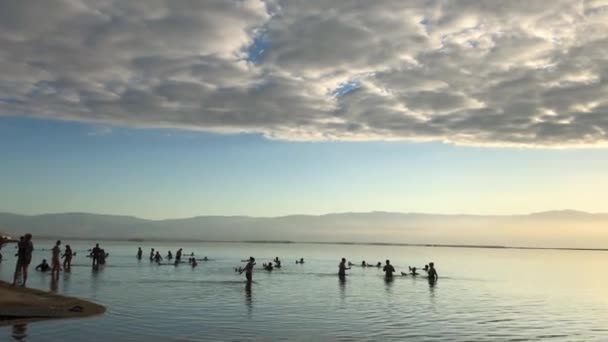 Az emberek a Holt-tengerben fürdenek Izraelben. Gyönyörű napfelkelte felhők — Stock videók