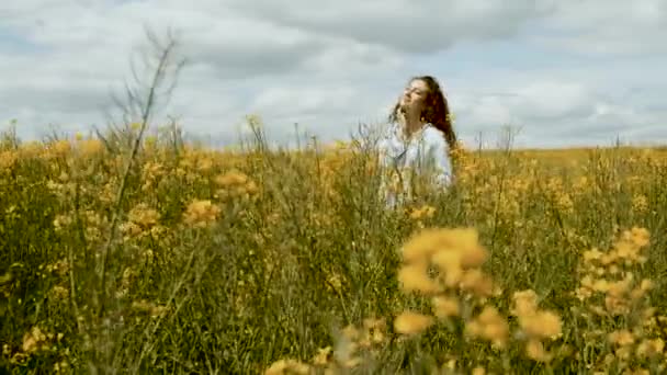 Cheerful girl of Caucasian appearance in rapeseed. Walks across the field in yellow flowers — Stock Video