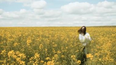 25 yaşında beyaz bir kadın sarı çiçeklerle doğada koşuyor.