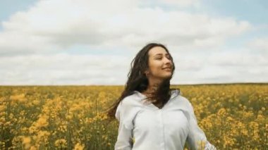 Baharda mutlu bir kız sarı kolza tohumu kameranın önünde koşar ve samimi bir şekilde gülümser. Sarı çiçekler güzel doğada