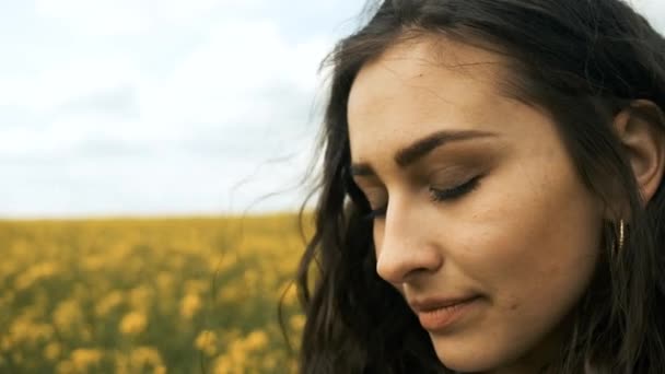 Menina feliz na primavera amarelo estupro posa na frente da câmera e sorri sinceramente. Flores amarelas na bela natureza — Vídeo de Stock