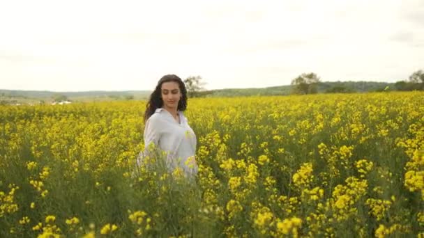 Fröhliches Mädchen kaukasischen Aussehens in Raps. Spaziergänge über das Feld in gelben Blumen — Stockvideo