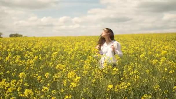 Cheerful girl of Caucasian appearance in rapeseed. Walks across the field in yellow flowers — Stock Video