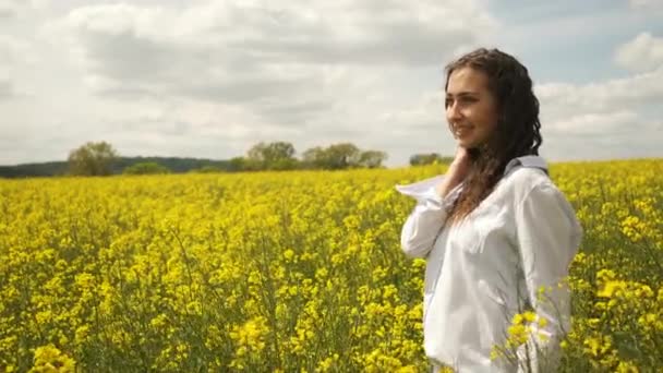 Cheerful girl of Caucasian appearance in rapeseed. Enjoys the nature of yellow flowers — Stock Video