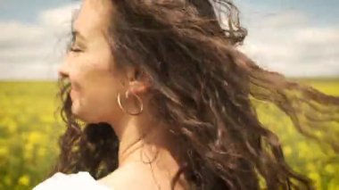 Mutlu kız, bahar sarısı kolza tohumu üzerinde kameranın önünde dönüyor.