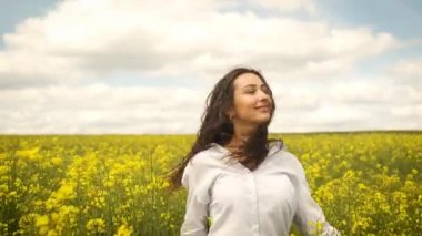 Baharda mutlu bir kız sarı kolza tohumu kameranın önünde koşar ve samimi bir şekilde gülümser. Sarı çiçekler güzel doğada