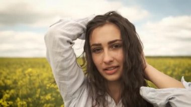 Baharda mutlu bir kız sarı kolza tohumu kameranın önünde koşar ve samimi bir şekilde gülümser. Sarı çiçekler güzel doğada