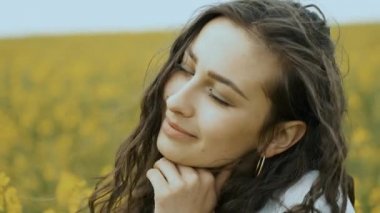 Sarı bahar tecavüzünde mutlu bir kız kameranın önünde poz verir ve samimi bir şekilde gülümser. Sarı çiçekler güzel doğada