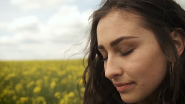 Gelukkig meisje in het voorjaar gele verkrachting poseert voor de camera en glimlacht oprecht. Gele bloemen op prachtige natuur — Stockvideo