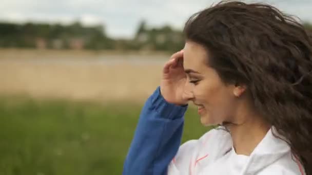 Atletisch jong meisje van blanke verschijning brunette loopt en communiceert met een partner in het park in de buurt van het meer — Stockvideo