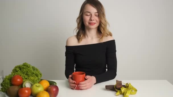 Uma nutricionista feminina não segue uma dieta adequada bebendo café com waffles multi-laríngeos. Ofochi e frutas na mesa — Vídeo de Stock