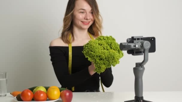Кавказька дівчинка, що тримає салат, залишає в руках і проводить онлайн-тренування. — стокове відео