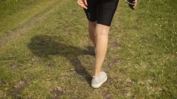 Beautiful cheerful brunette girl running in the park near the lake listens to music on headphones — Stock Video